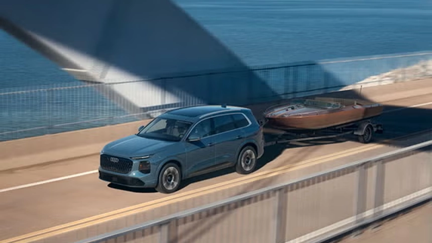 Blue Audi Q7 towing a wooden boat on a trailer across a bridge