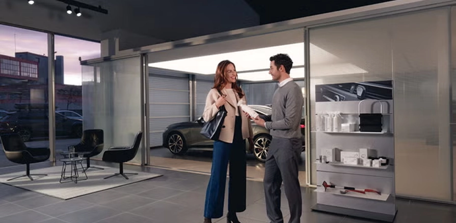 Two people talking in an Audi showroom with a vehicle displayed behind the glass