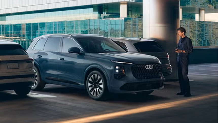 Person standing beside a gray Audi Q7 using a smartphone in a parking structure