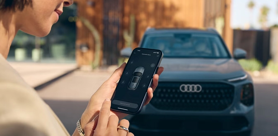 Person using the myAudi app on a smartphone with a gray Audi Q7 in the background
