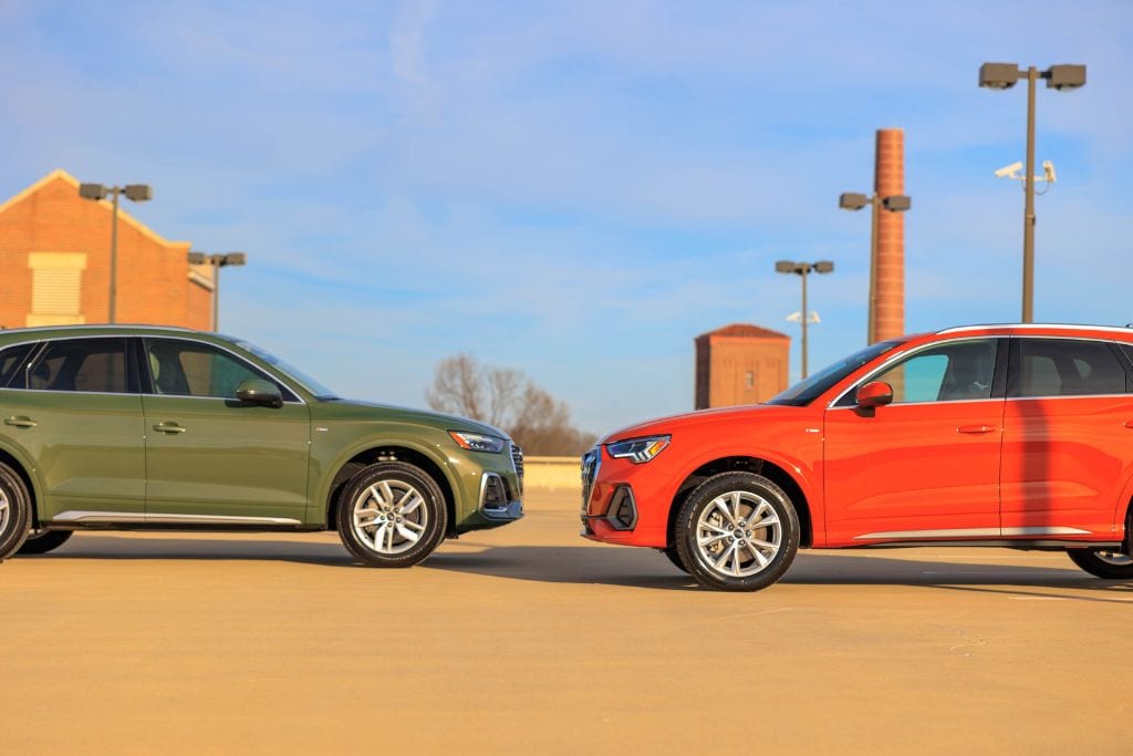 audi-suv-for-sale-nc.jpg Side view of 2024 Audi SUV models, including an orange Audi Q3 and a green Audi Q7, parked facing each other atop a parking deck