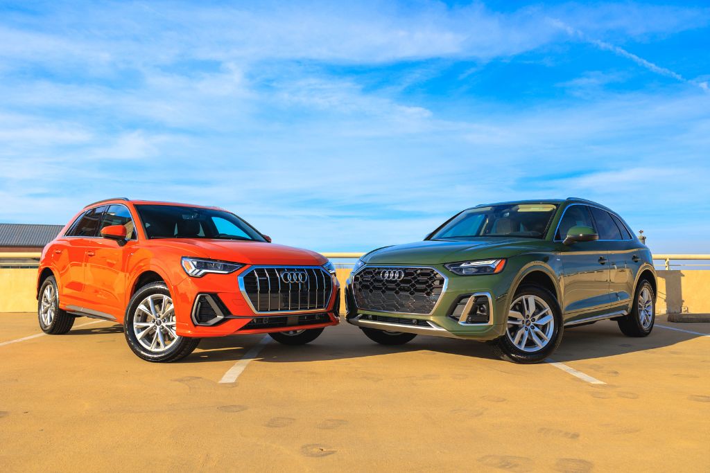 audi-q3-q5-suv.jpg Audi SUV models, including an orange Audi Q3 and a green Audi Q7, parked facing each other atop a parking deck