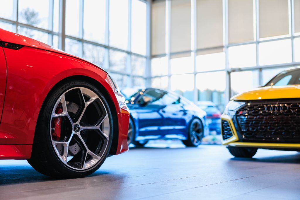 audi-warrnty-information.jpg Close up view of wheel on red Audi sportscar, with both a blue Audi car and yellow Audi car visible in the background, inside the showroom within an Audi dealership