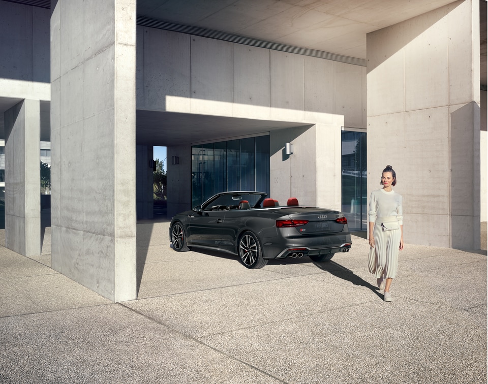 2022-Audi-S5-Prestige-SSportPackage-Sedan-L02.png dark gray Audi S5 convertible parked in a modern parking garage with the driver walking away