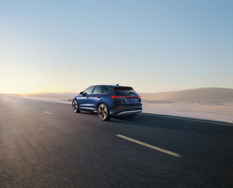 2022-Audi-Q4-Prestige-WheelAddOn-SUV-L03.png blue Audi Q4 electric SUV driving on a desert road at dusk