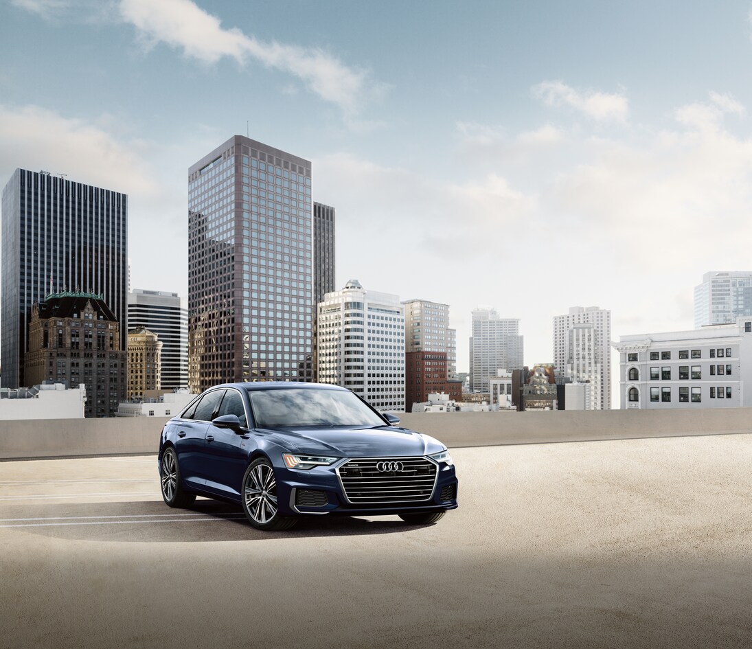 2022-Audi-A6-55TSI-PremiumPlus-WheelAddOn-Sedan-L06.png black Audi A6 parked on a structure overlooking a city skyline