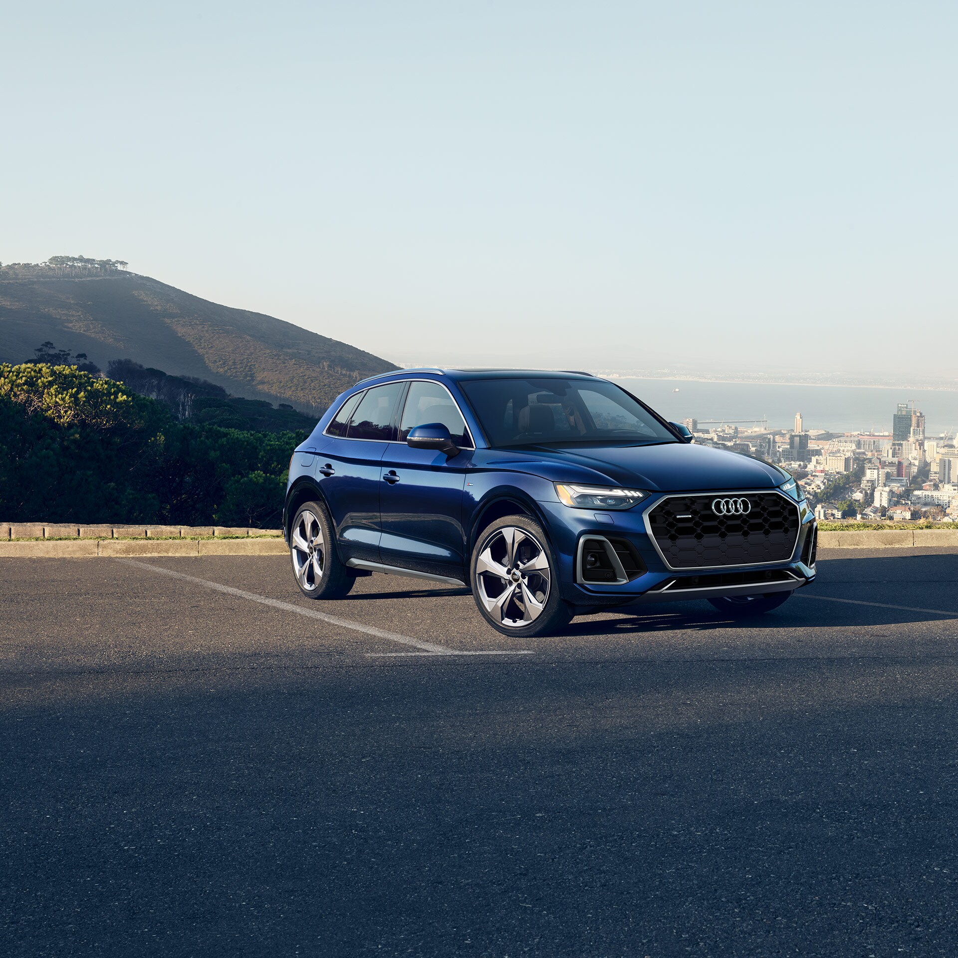 dark blue Audi Q5 SUV parked in a lot overlooking hills and a cityscape