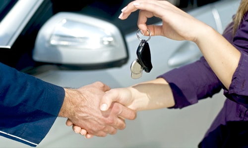 Closeup of man and woman shaking hands while handing over car keys