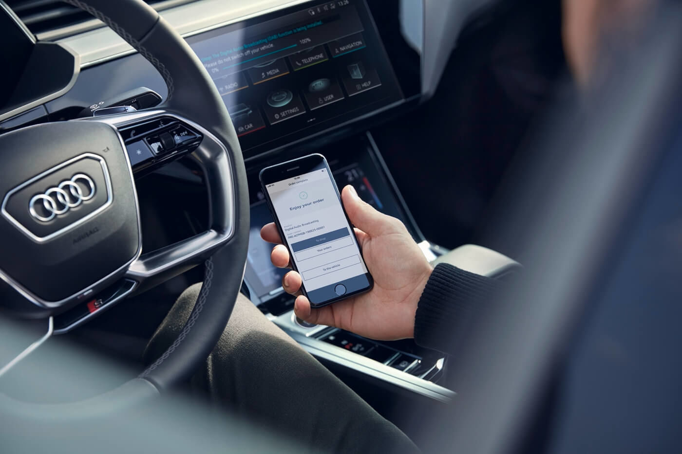 Propriétaire d'Audi à l'intérieur du véhicule téléchargeant l’application MyAudi sur téléphone mobile