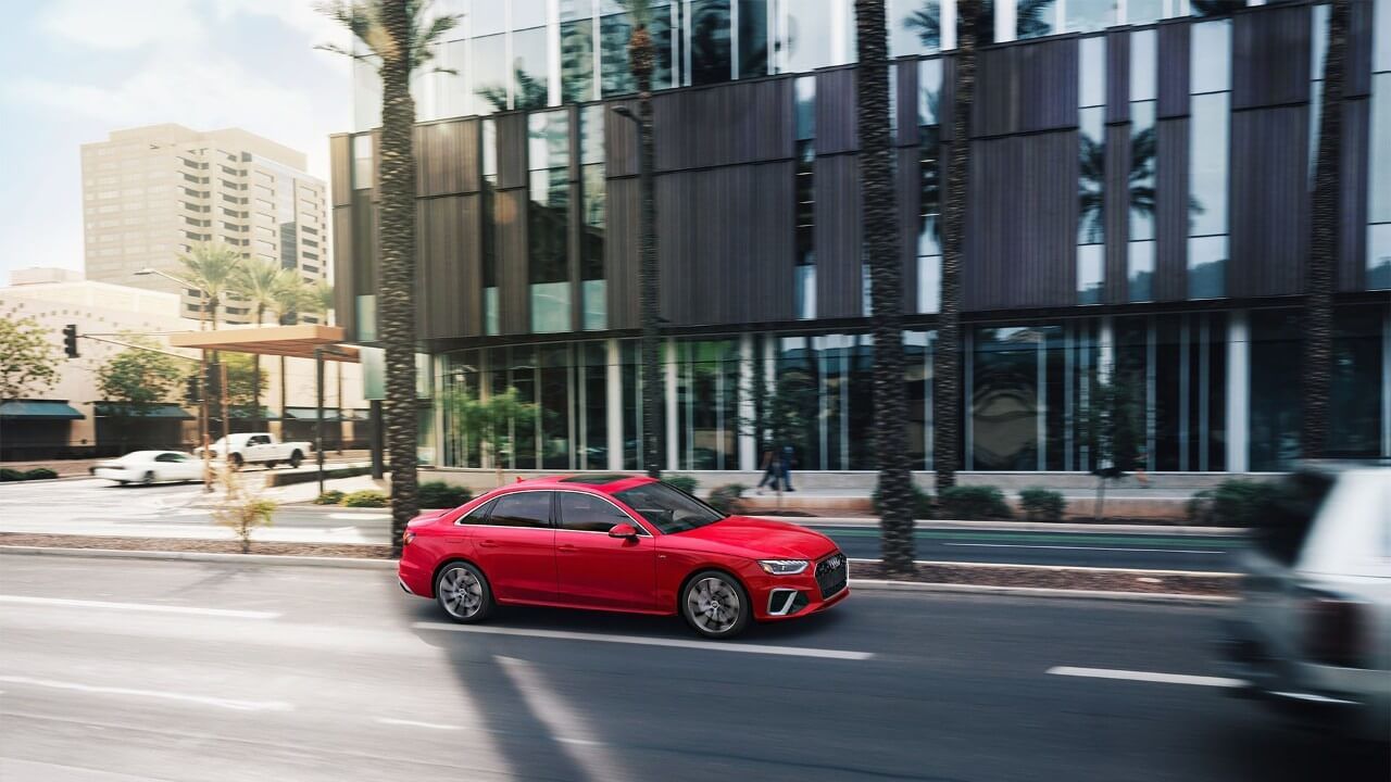 Vue latérale d'une berline Audi A4 rouge roulant sur un boulevard en ville