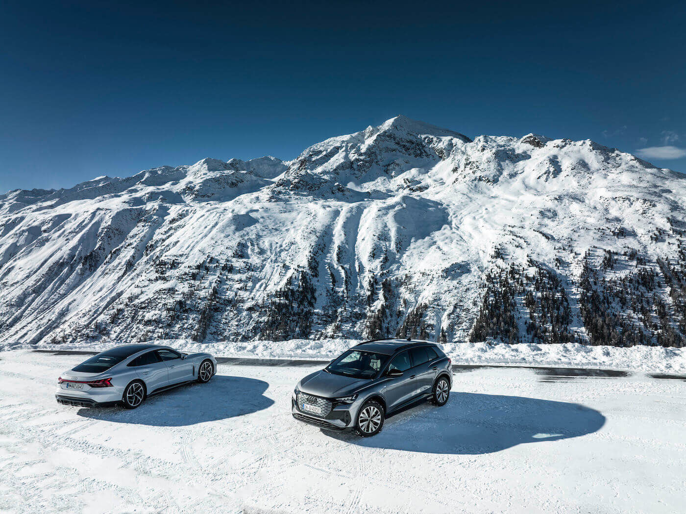 Un Audi e-tron GT quattro et un Q4 50 e-tron quattro Edition One garés sur une terre glacée face à une montagne enneigée