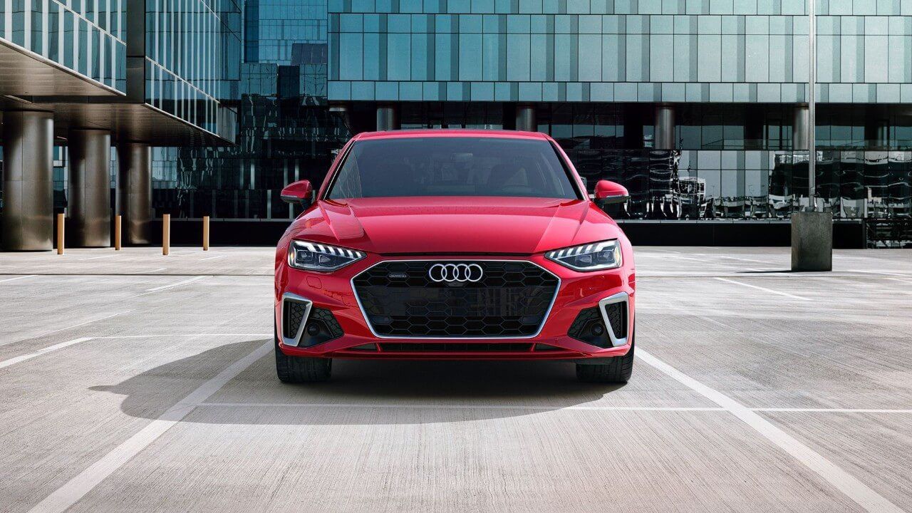 Vue avant d'une berline Audi A4 rouge garée dans un stationnement d'un édifice