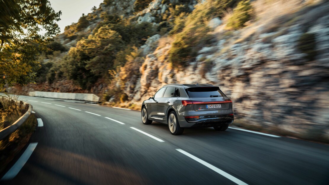 vue latérale arrière d'une Audi Q8 e-tron 2023 sur une route le long d'une paroi rocheuse