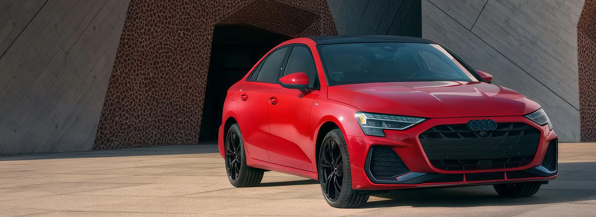 Red 2026 Audi A3 parked beside a concrete building at dusk, seen from the front three-quarter angle