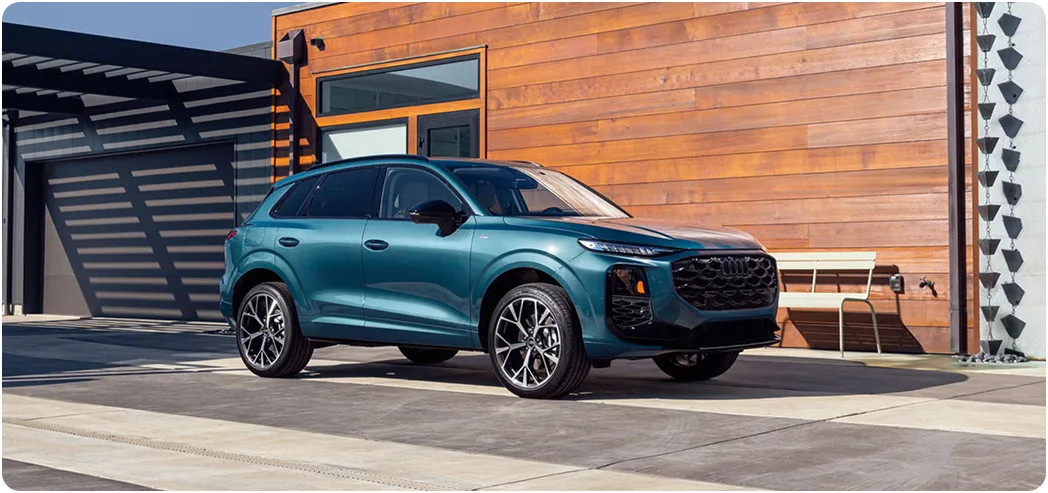 Teal Audi Q3 parked beside a wood-clad building, seen from the front three-quarter angle