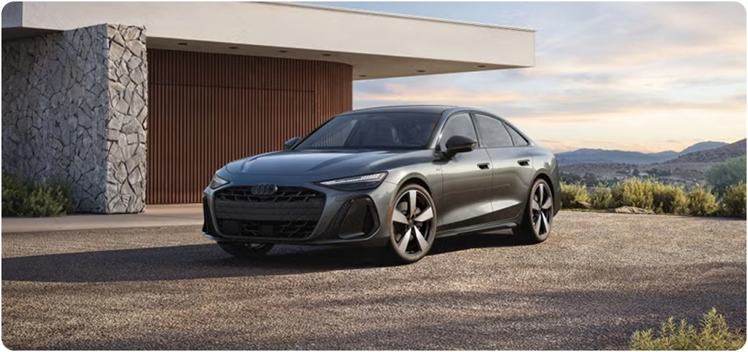 Grey Audi A6 Sedan parked on gravel outside a modern stone house at sunset