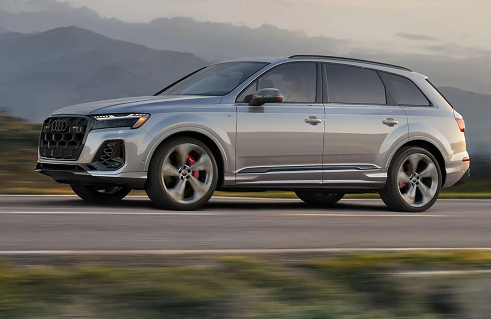 A silver Audi Q7 SUV driving along a highway with mountains behind it
