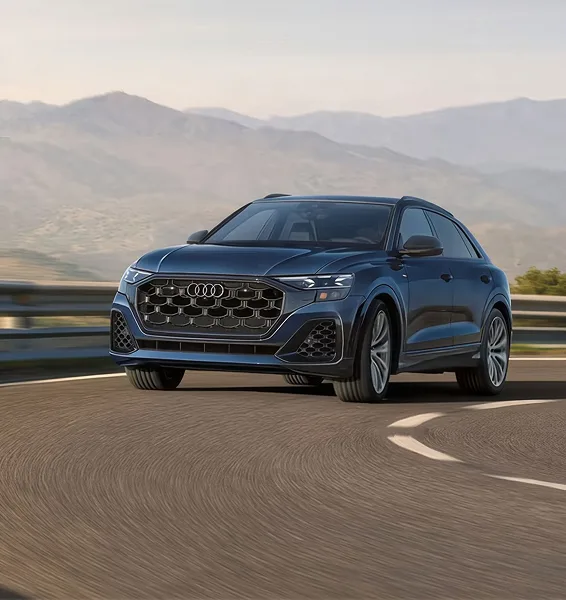 Blue Audi Q8 cornering on a mountain road with hills in the distance