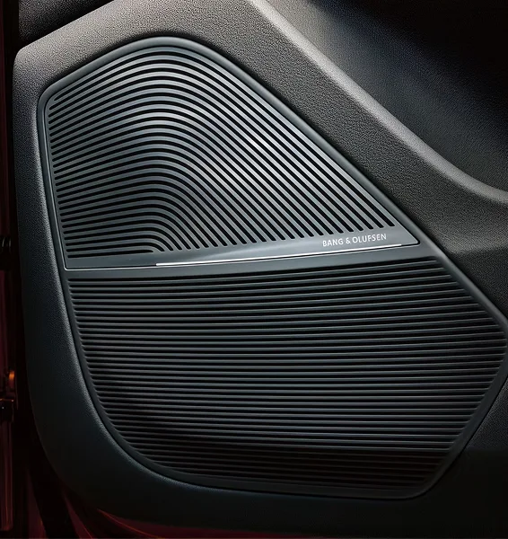 Close-up of a Bang & Olufsen speaker grille set into the red-lit door trim of the Audi Q8