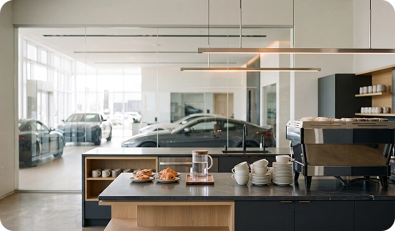 The Audi Stuart customer café counter set with an espresso machine, stacked white cups and fresh pastries, looking out over the showroom