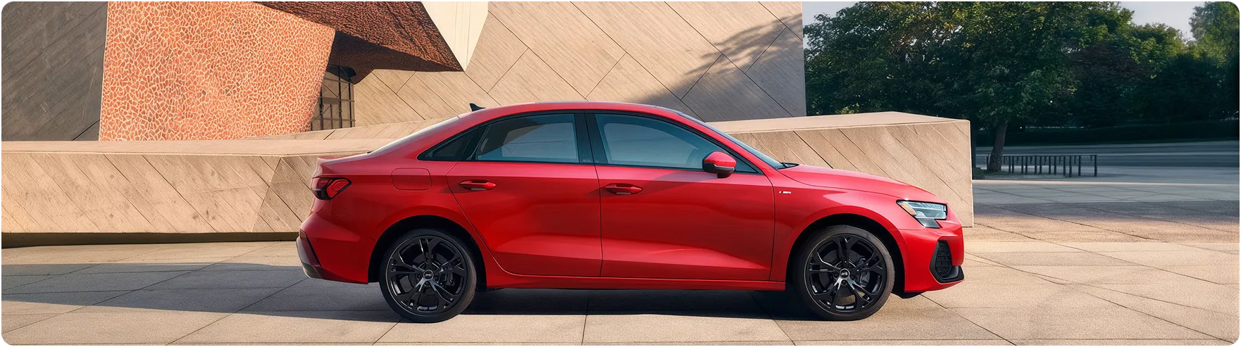 Red Audi A3 seen in profile outside a modern concrete building