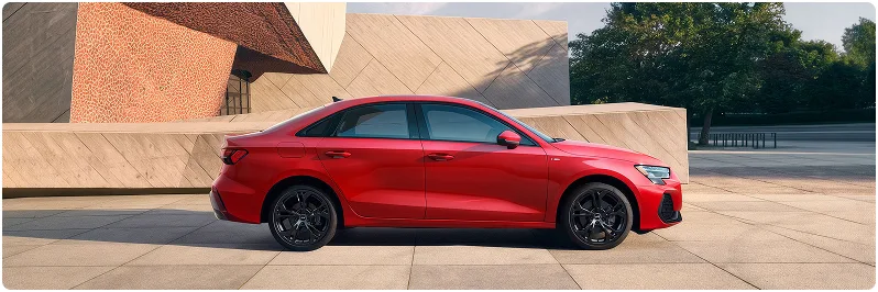 Red Audi A3 seen in profile outside a modern concrete building