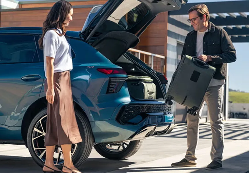Two people loading luggage into the open tailgate of a teal Audi Q3