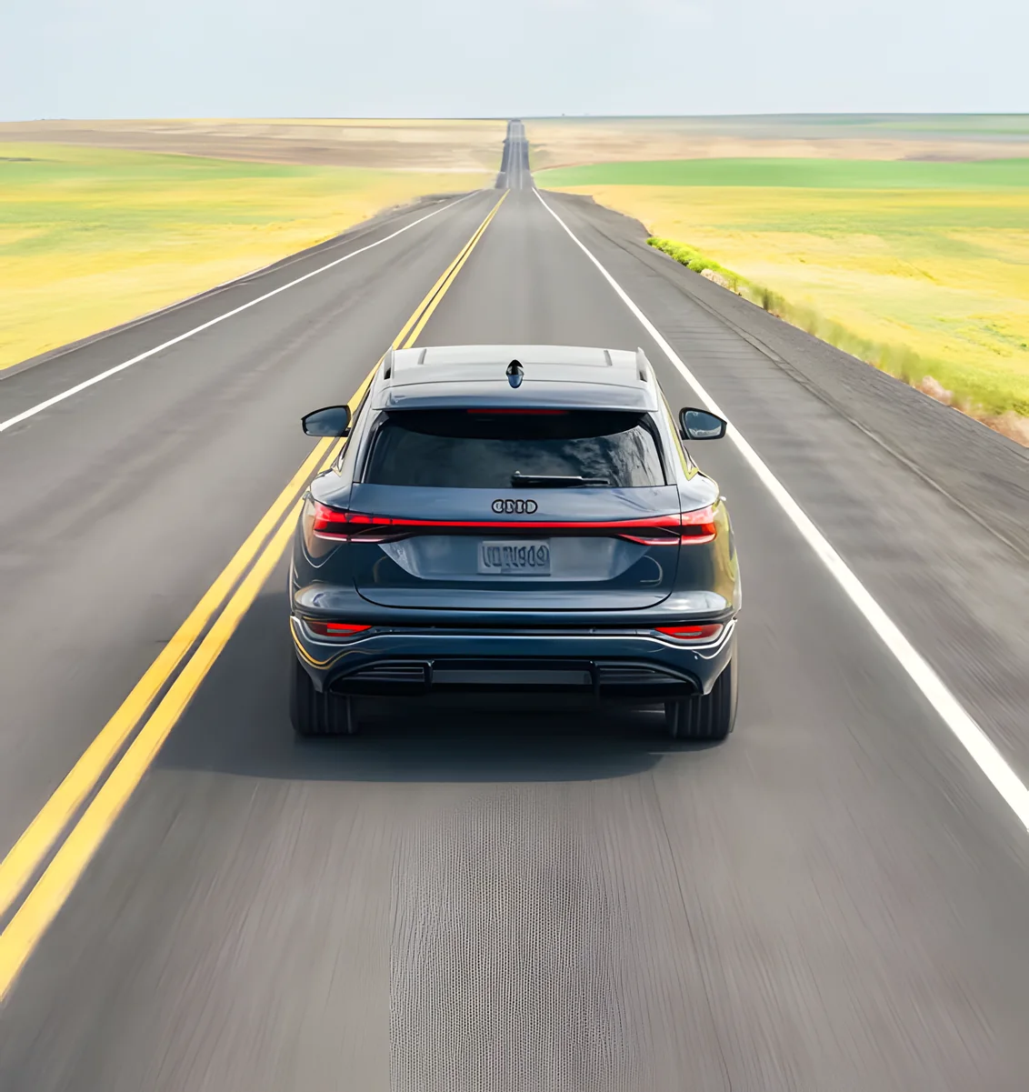 Audi Q6 e-tron driving down a long straight road through open fields