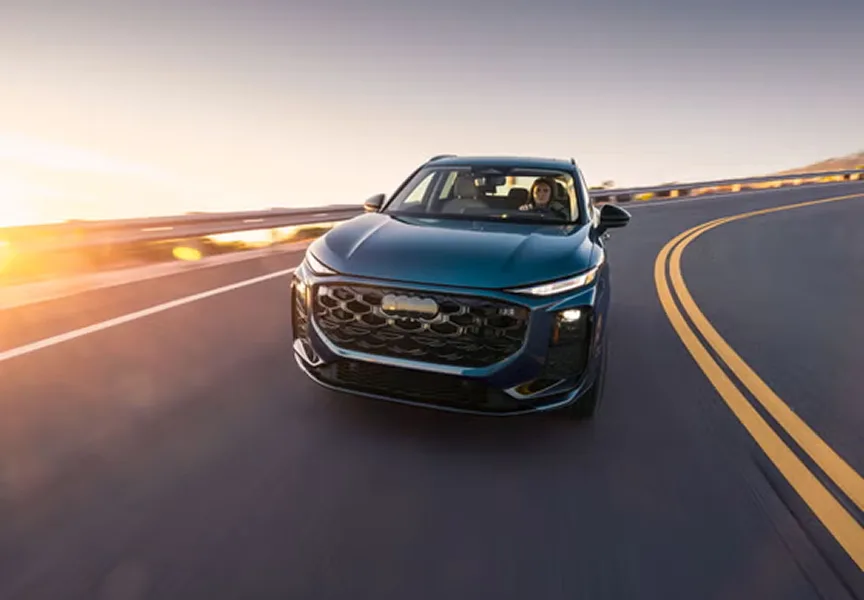Blue Audi Q3 driving a highway curve at sunset, seen from the front