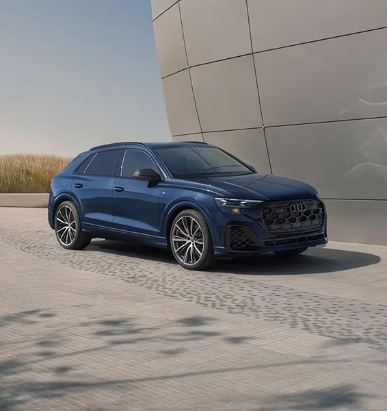 Blue Audi Q8 parked beside a curved metal-clad building, seen from the front three-quarter angle