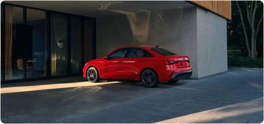 Red Audi A3 parked beside a dark glass building, seen from the rear three-quarter angle
