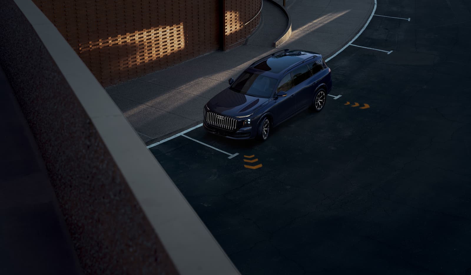 2027 Audi Q9 seen from above, parking in a space beside a brick building