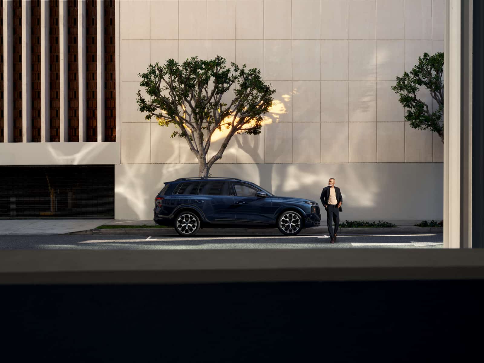 2027 Audi Q9 side view parked on a city street, with a man standing beside the front