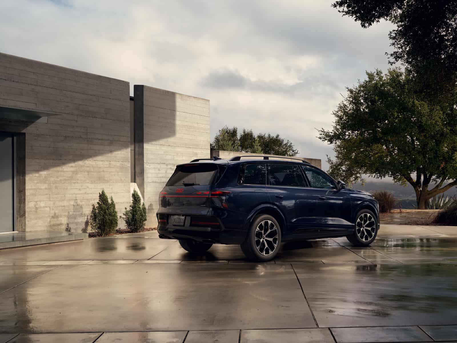 2027 Audi Q9 rear three-quarter view parked on wet concrete outside a modern home