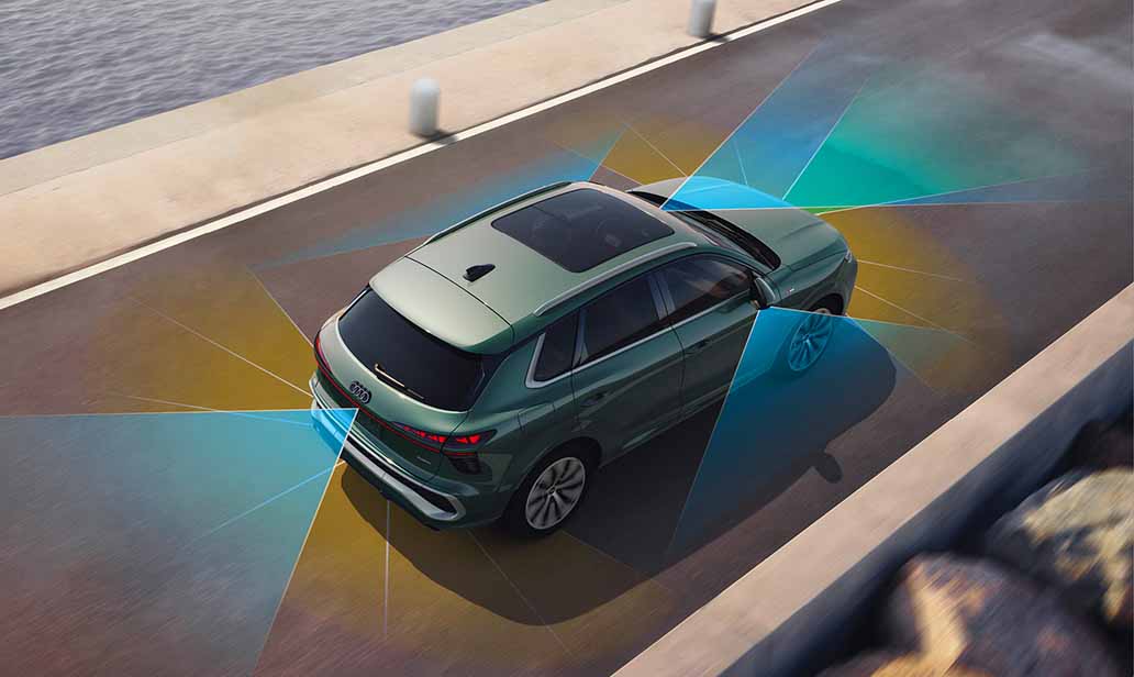 Audi Q3 displaying surround-view and lane detection sensors in action, illustrating advanced driver-assistance technologies while driving along a scenic coastal road.