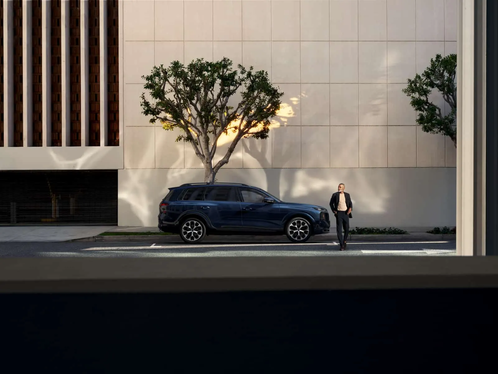 2027 Audi Q9 side view parked on a city street, with a man standing beside the front