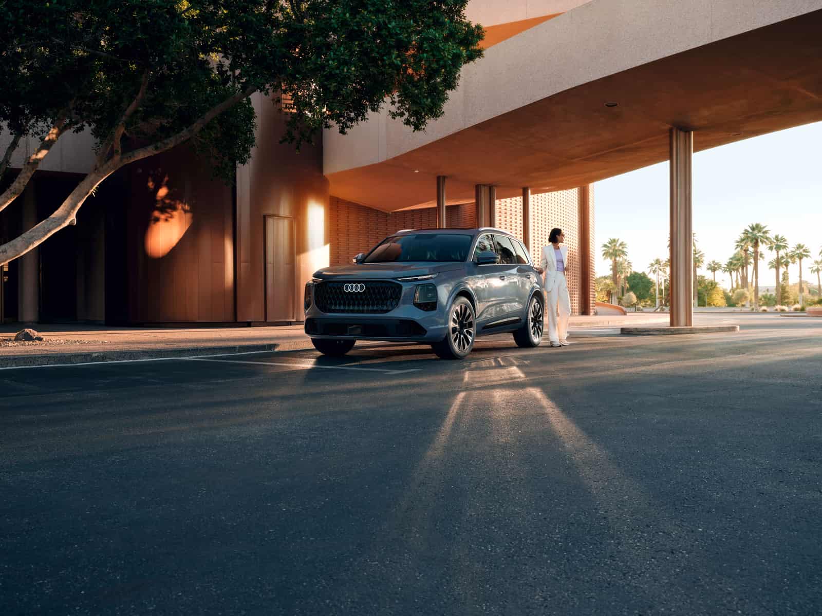 2027 Audi Q7 parked outside a modern building at sunset, front three-quarter view