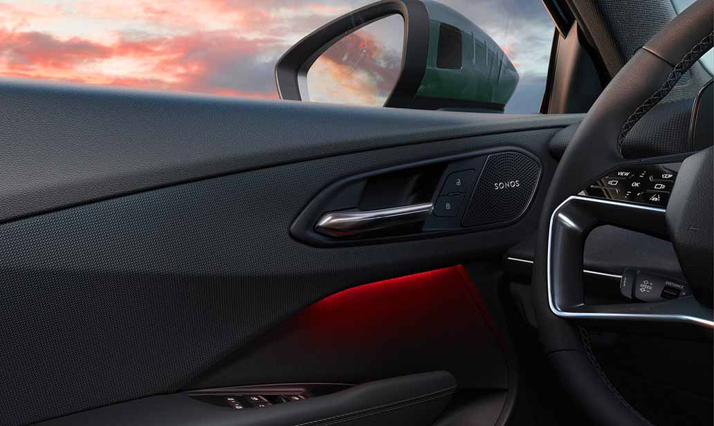 Detail of Audi Q3 front door panel featuring Sonos speaker grille, illuminated ambient lighting, and upscale stitching against a vibrant sunset reflection.