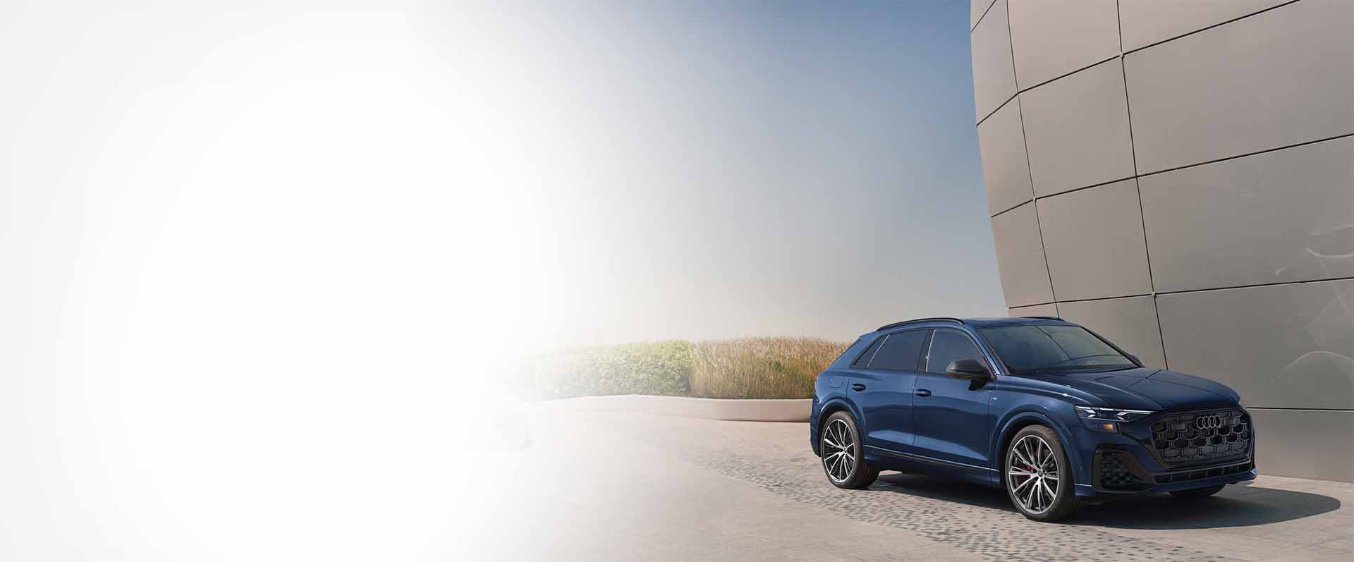Blue Audi Q8 parked beside a curved metal building