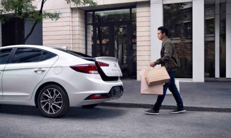 2020 Hyundai Elantra in white parked on the side of the street with trunk opening and someone walking up to it with bags
