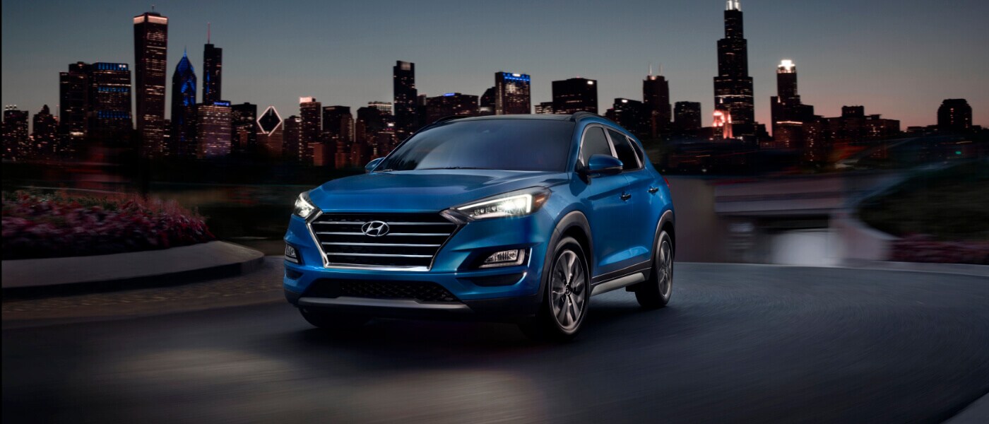 2020 Hyundai Tucson in blue driving on curve at night with the chicago skyline behind it