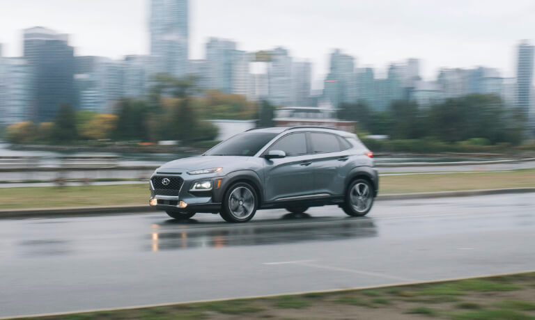 Silver 2020 Hyundai Kona driving on a road in the rain against a city skyline
