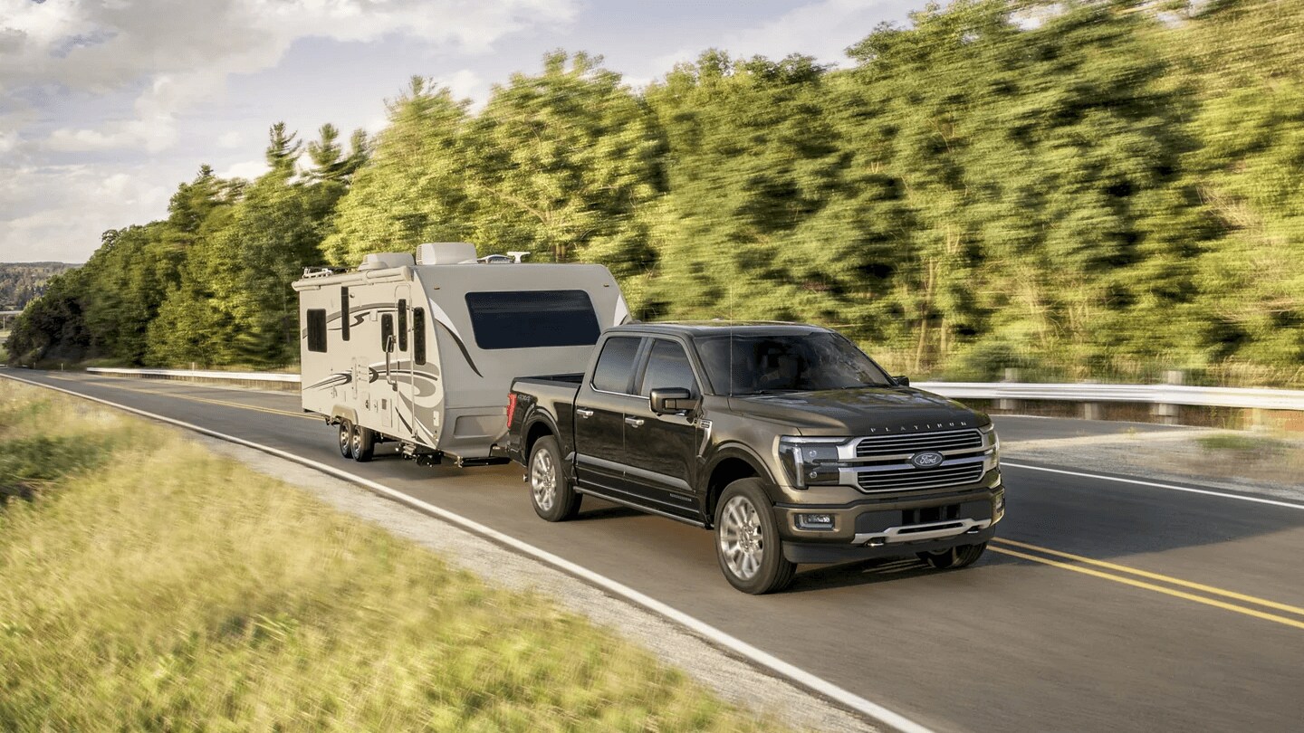 The Ford F-150 is a versatile family vehicle with modern comfort & technology features Exterior shot of a Ford F-150 driving down a highway, towing an RV trailer