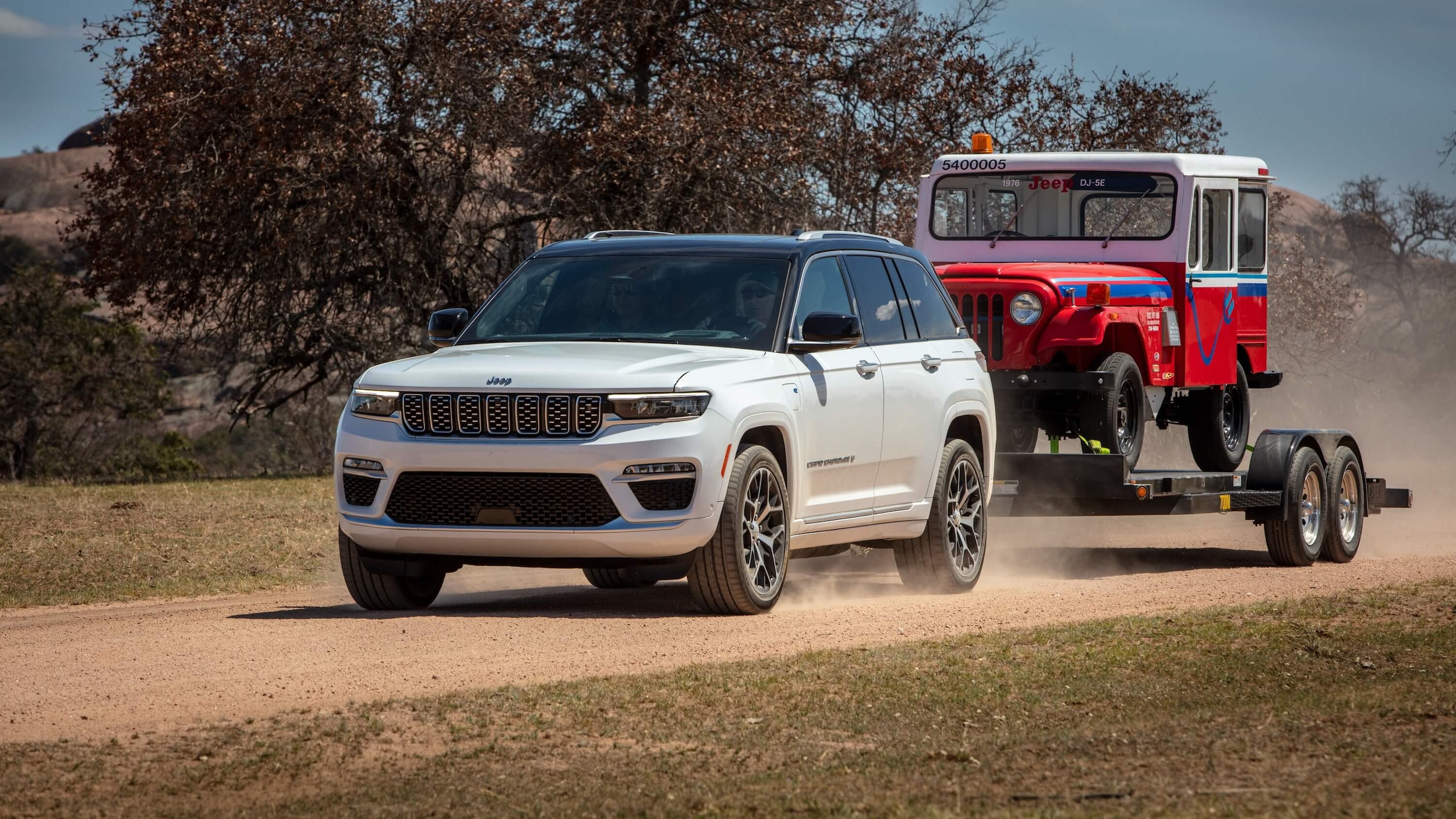 Learn about the performance features of the Jeep Grand Cherokee 4xe A white Jeep Grand Cherokee 4xe towing a flat trailer with a red Jeep Wrangler on top