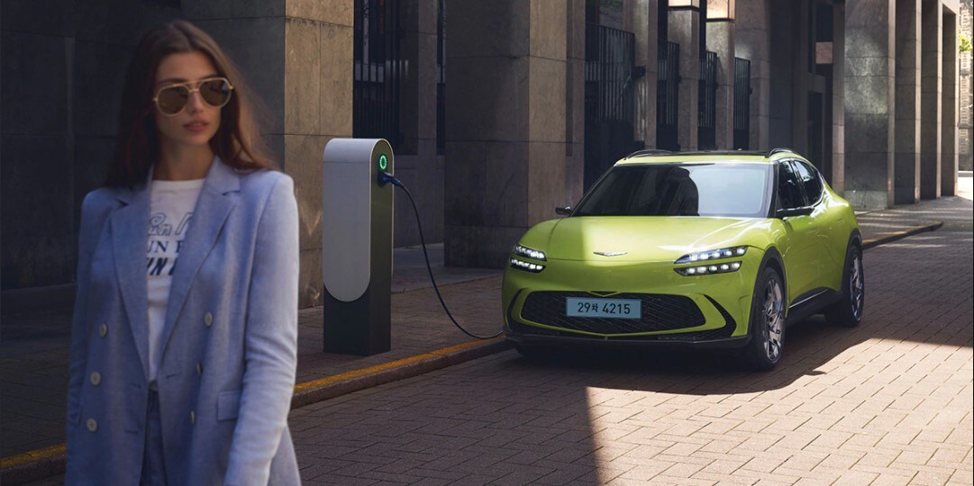 Learn more about Genesis EVs at Genesis of West Columbia Genesis electric vehicle in a city; woman walking away in sunglasses