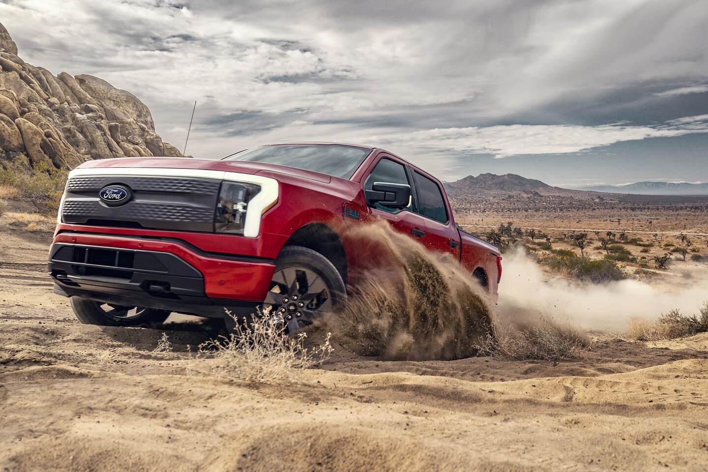 An image showing the a red Ford F-150 Lightning off-roading through some dirt