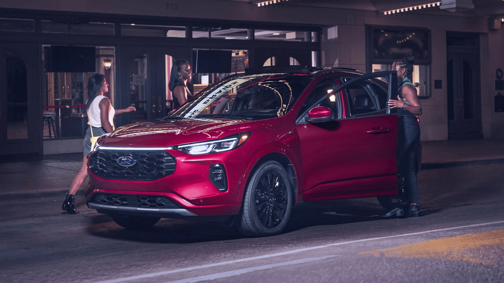 Learn which Ford SUVs are ideal for driving in the city Rapid Red Ford Escape parked in front of a city building with three adult women entering the SUV
