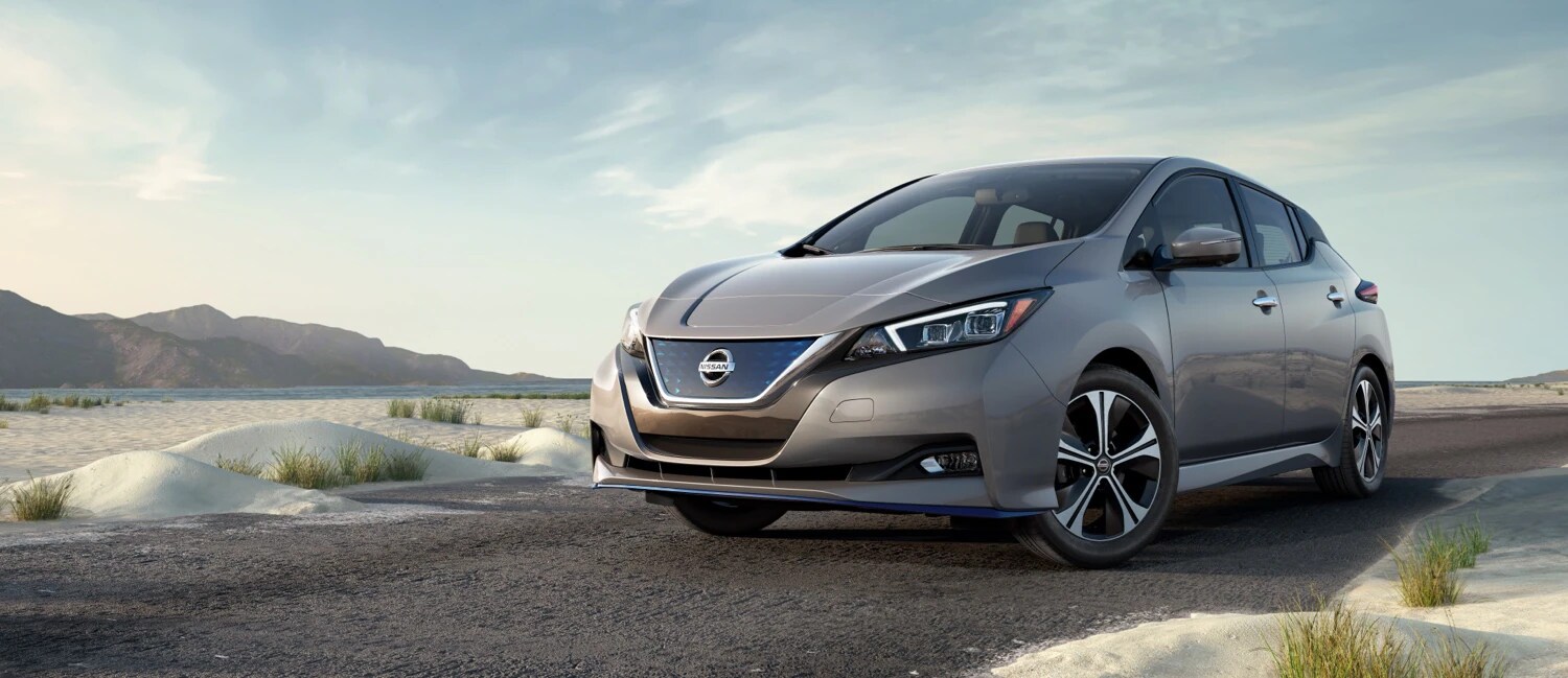 Learn more about whether a hybrid or electric vehicle is right for you at AutoNation Nissan Marietta Grey Nissan Leaf in the desert near mountains on a partially cloudy day.