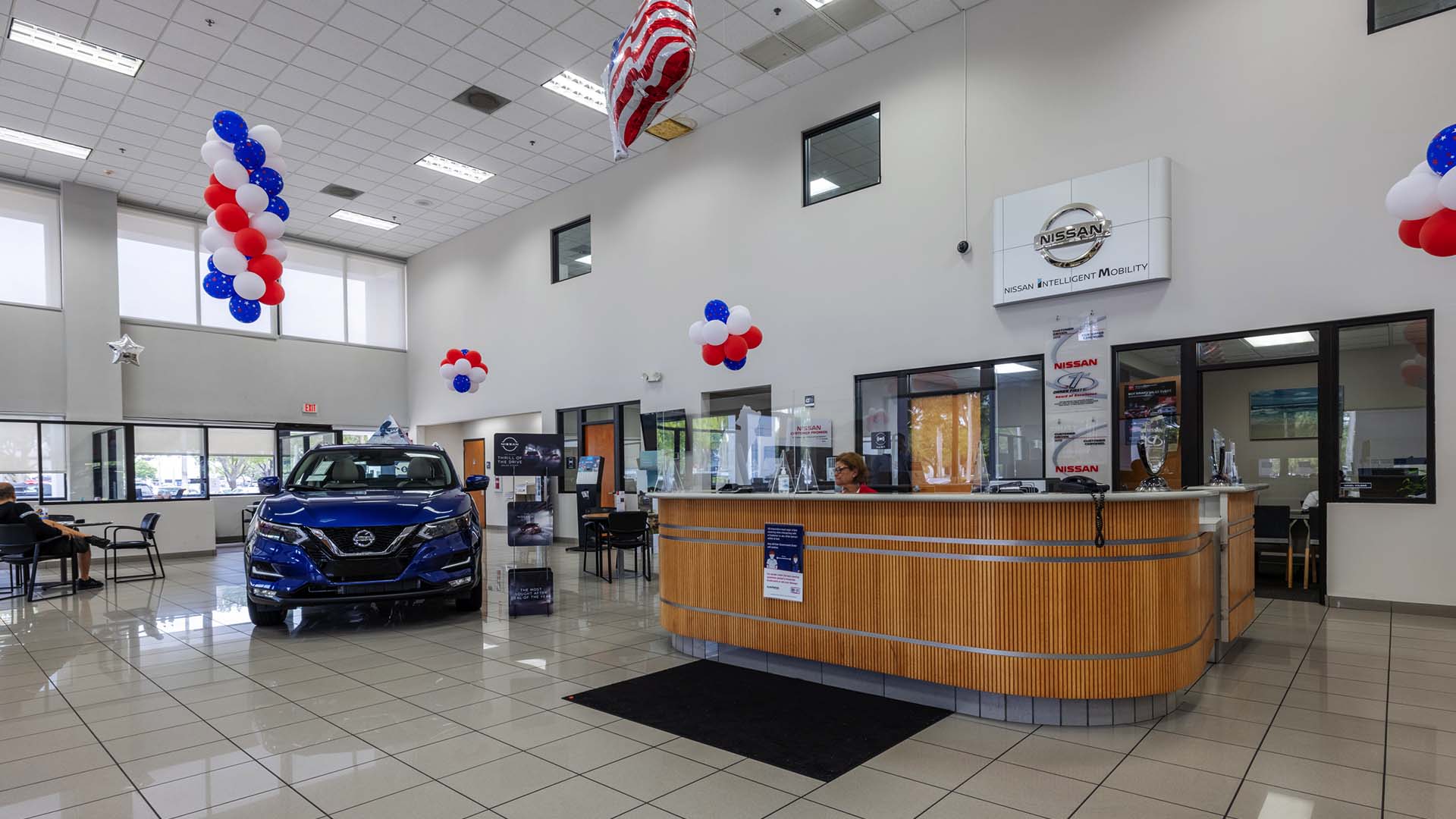 Find out about financing at AutoNation Nissan Pembroke Pines Interior view of AutoNation Nissan Pembroke Pines, with a view of a blue Nissan and large desk