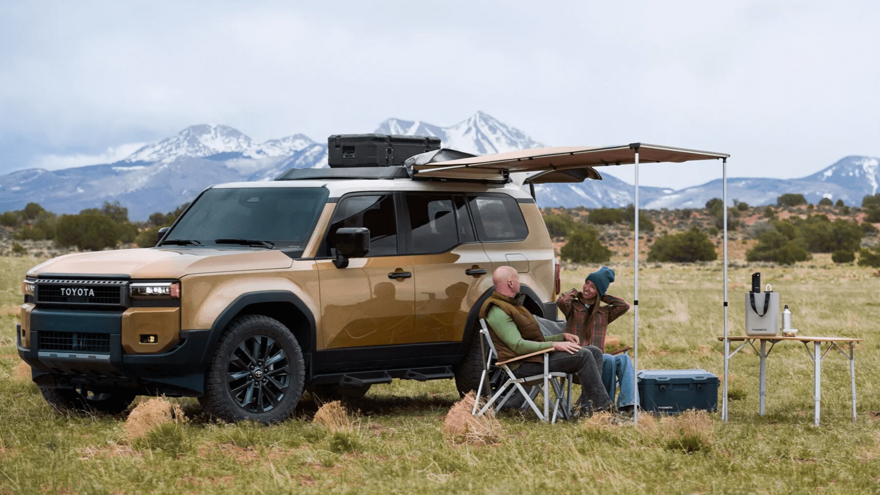 Learn about the specs & features of the Toyota Land Cruiser Outdoor shot of a Toyota Land Cruiser used as a campsite with two adults sitting under canopy that's attached to the side of the Land Cruiser